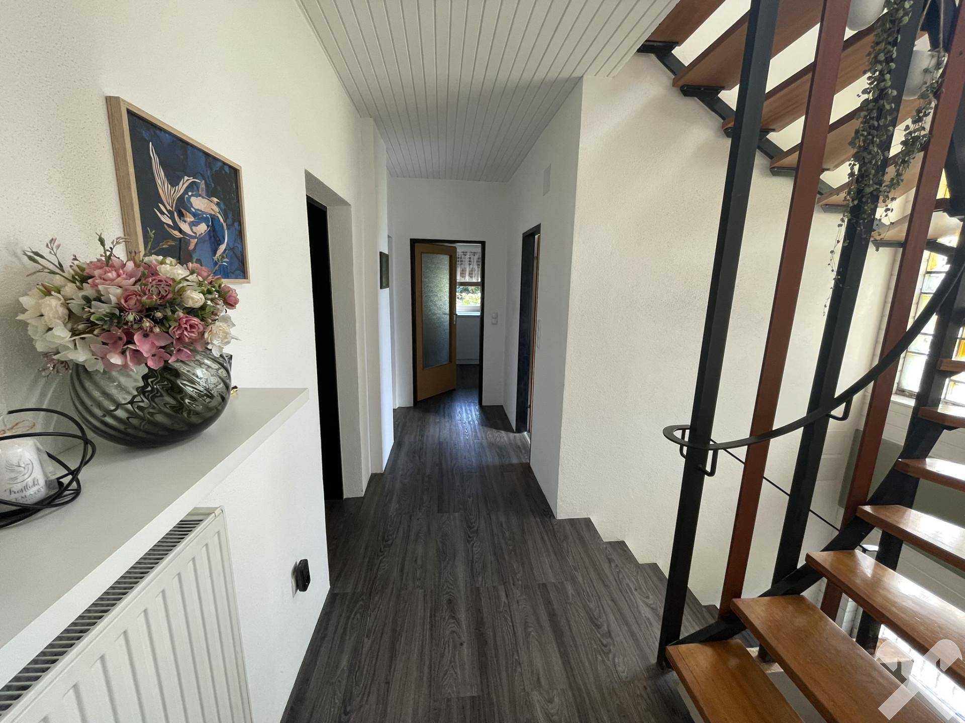 Heller Flur mit modernem Laminatboden und offener Holztreppe zum Obergeschoss.
