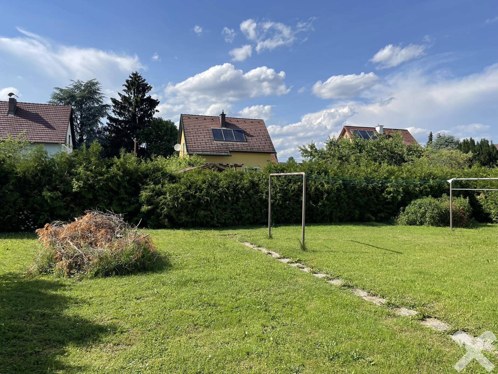 Großer, sonniger Gartenbereich mit Rasenfläche und hohen Hecken, umgeben von weiteren Wohnhäusern.