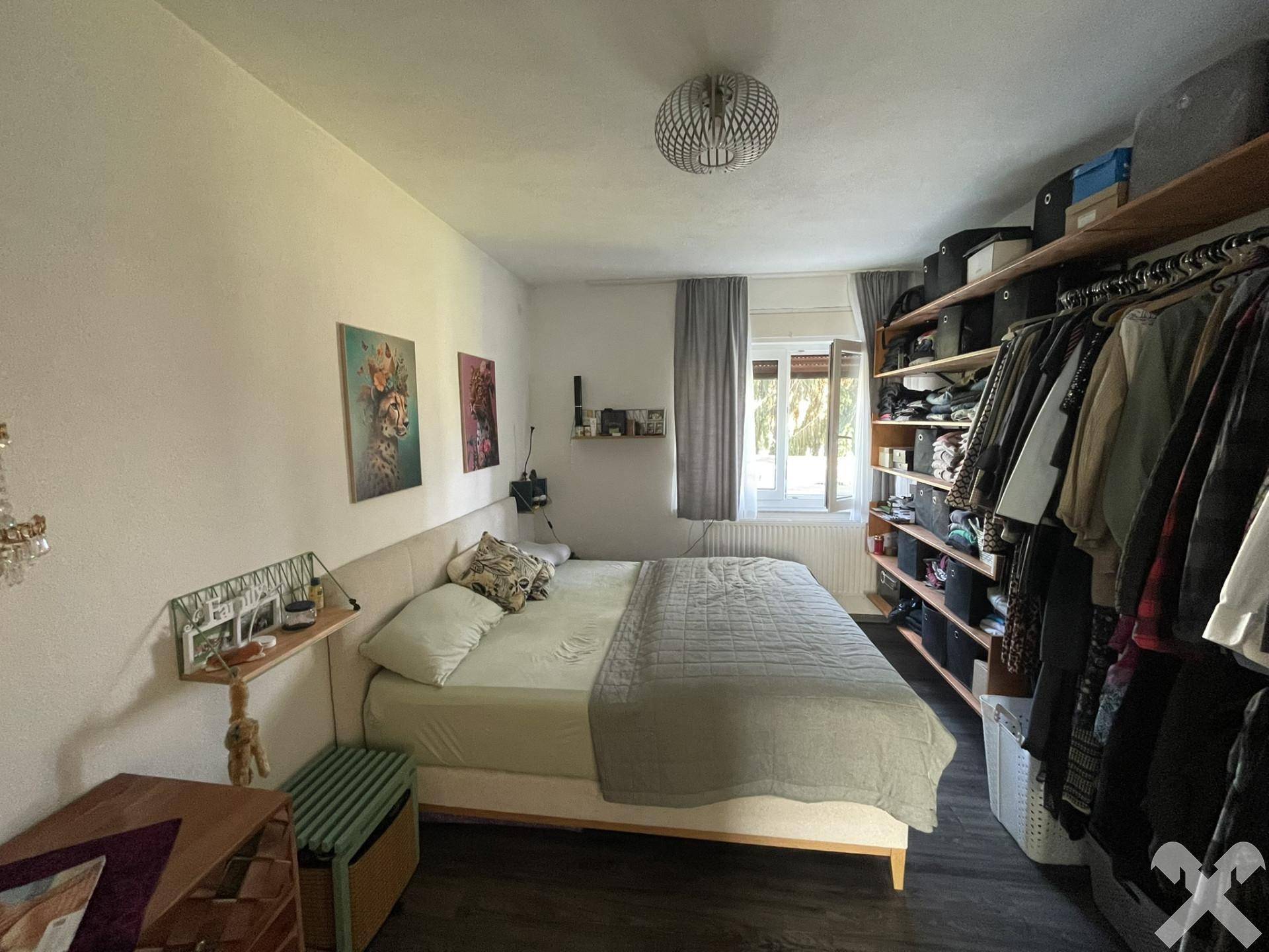 Schlafzimmer mit dunklem Laminatboden, Doppelbett und offenem Kleiderschrank, hell und funktional.