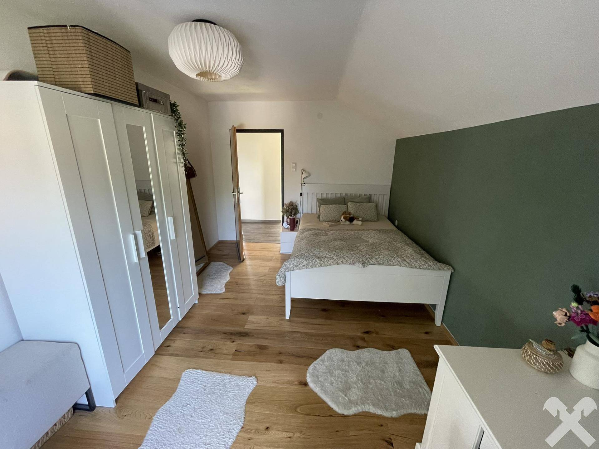 Schlafzimmer mit Holzboden, weißem Bett und Kleiderschrank, mit grüner Akzentwand.