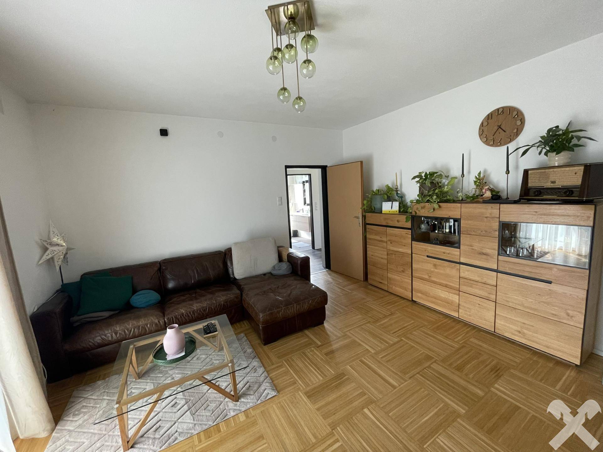 Gemütliches Wohnzimmer mit Parkettboden, Ledersofa und Holzmöbeln, hell und einladend gestaltet.