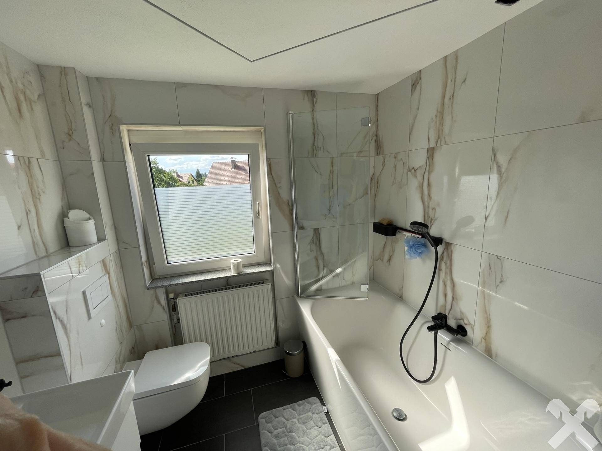 Modernes Badezimmer mit Badewanne, Dusche und Fenster, gefliest mit Marmoroptik.
