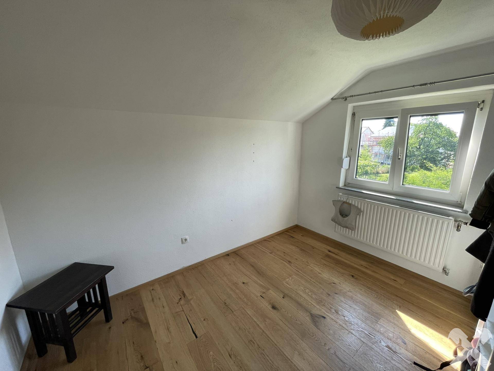 Leeres Zimmer mit Holzboden und Fenster, bereit zur individuellen Gestaltung.