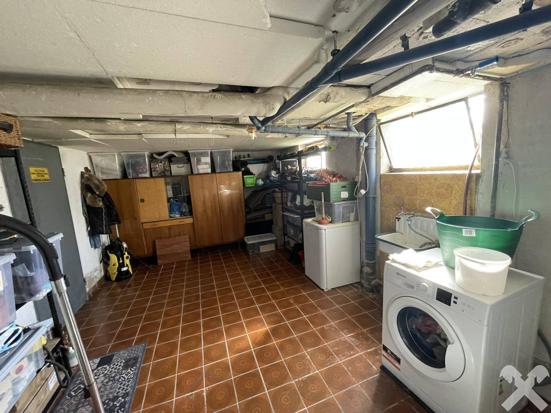 Kellerraum als Waschküche mit Waschmaschine, Fliesenboden und kleinem Fenster.