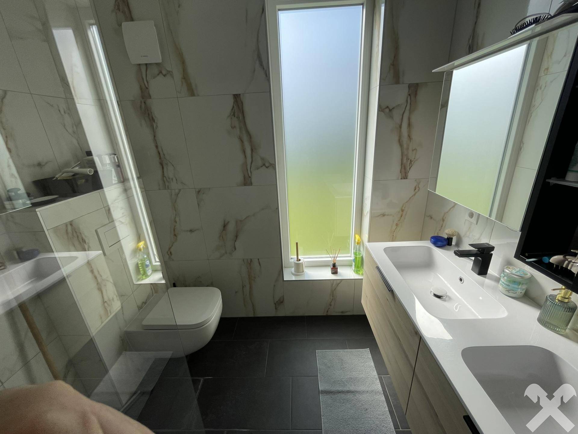 Modernes Badezimmer mit großformatigen Marmorfliesen, Doppelwaschbecken und wandhängendem WC.