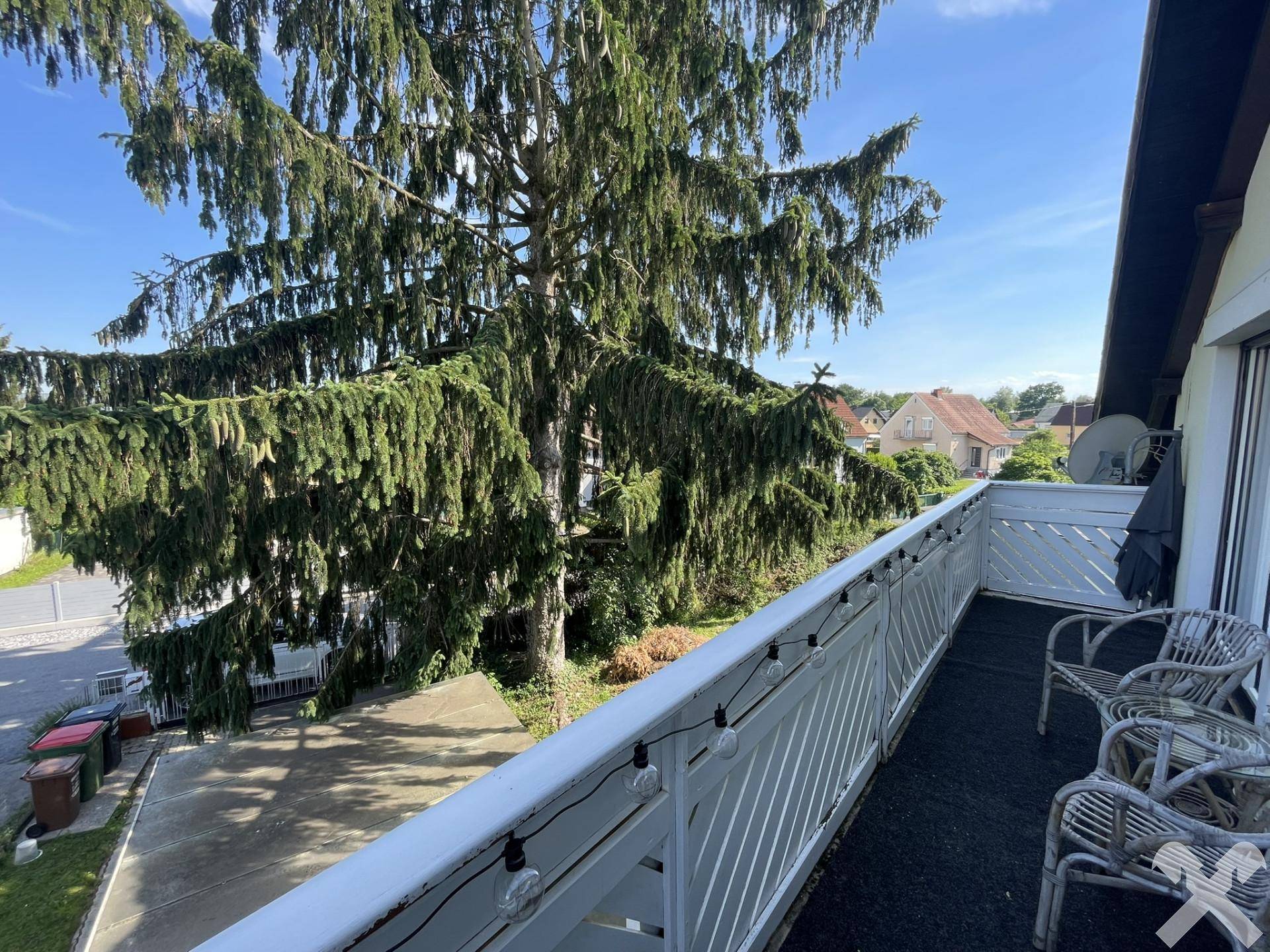 Geräumiger Balkon mit Sitzgelegenheiten und Blick auf die Umgebung und Bäume.
