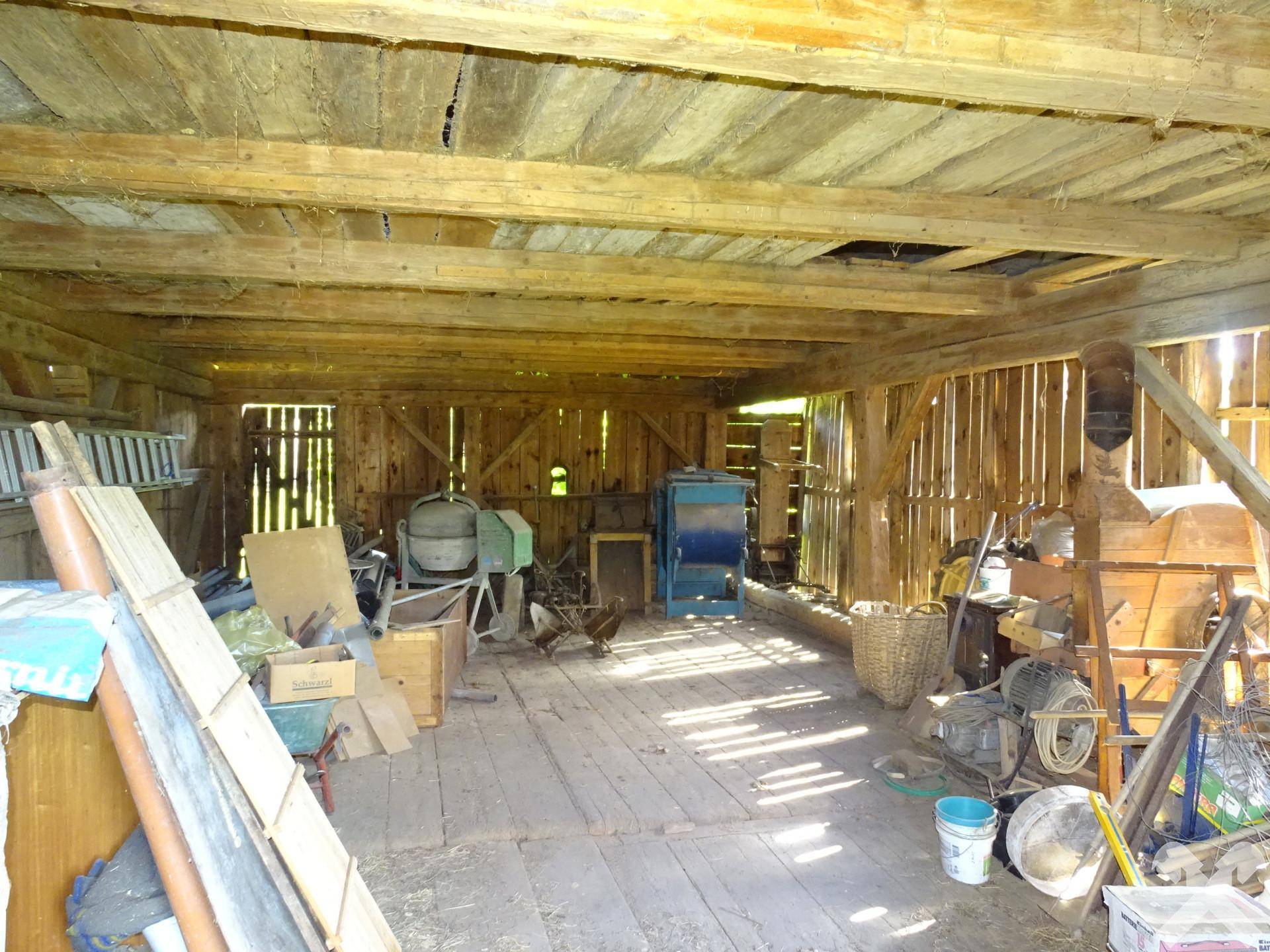 Geräumiger Werkstattraum mit Holzboden, sichtbaren Deckenbalken und verschiedenen Geräten und Materialien.