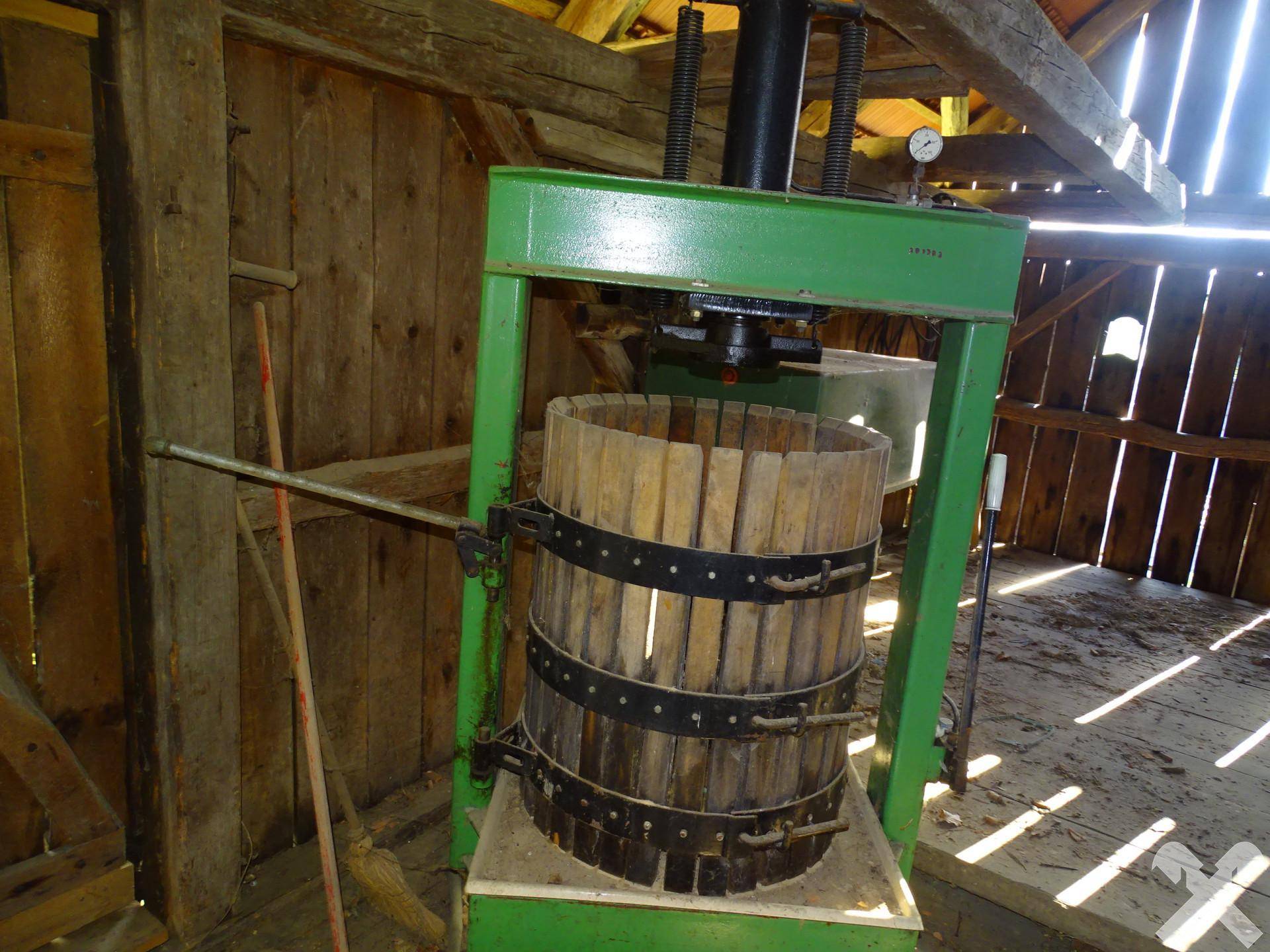 Historische hölzerne Weinpresse in einem rustikalen Raum mit Holzwänden und natürlichem Lichteinfall.