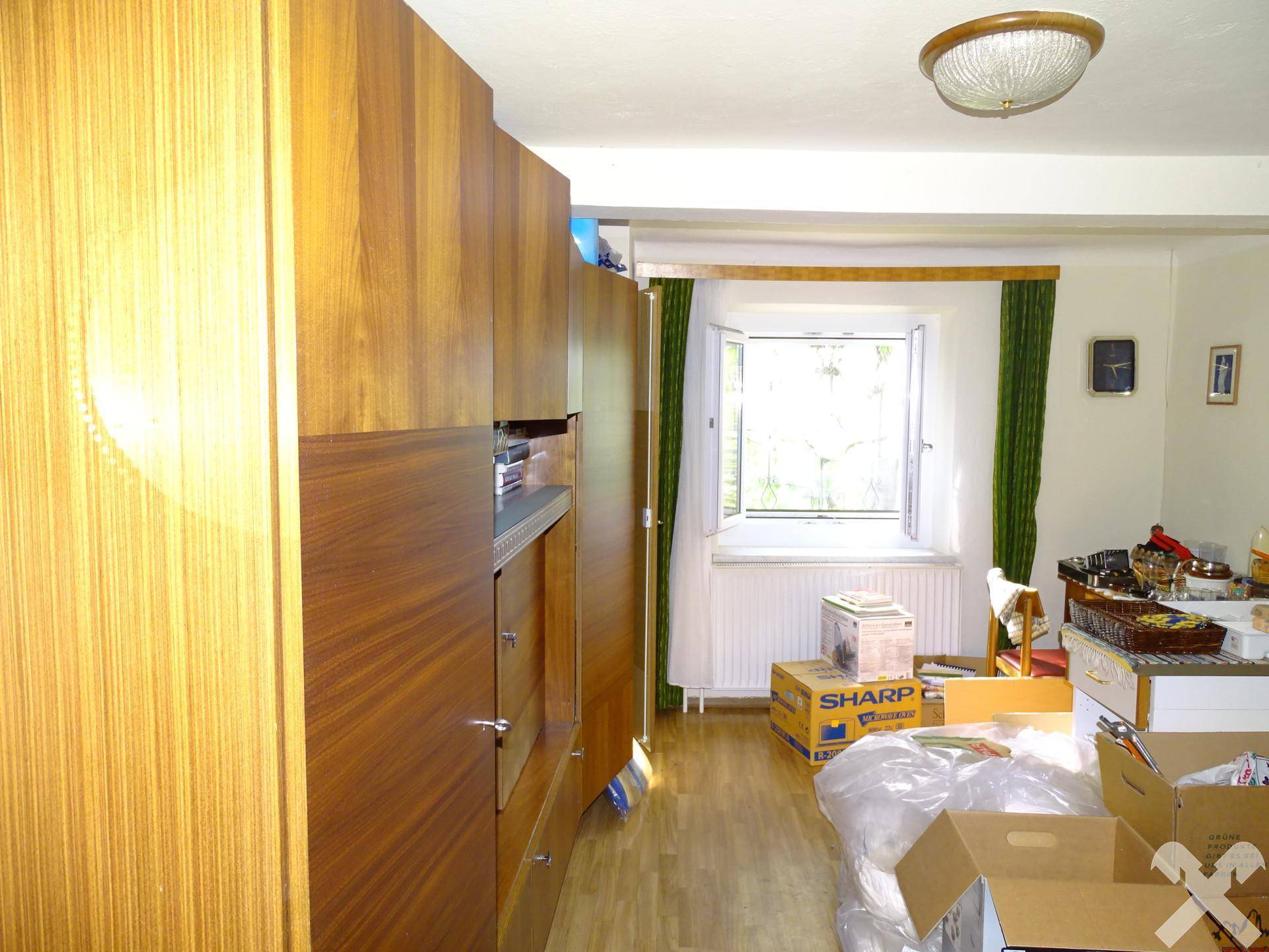 Innenraum mit großem Holzschrank, Fenster und Umzugskartons, die auf eine bevorstehende Nutzung hindeuten.