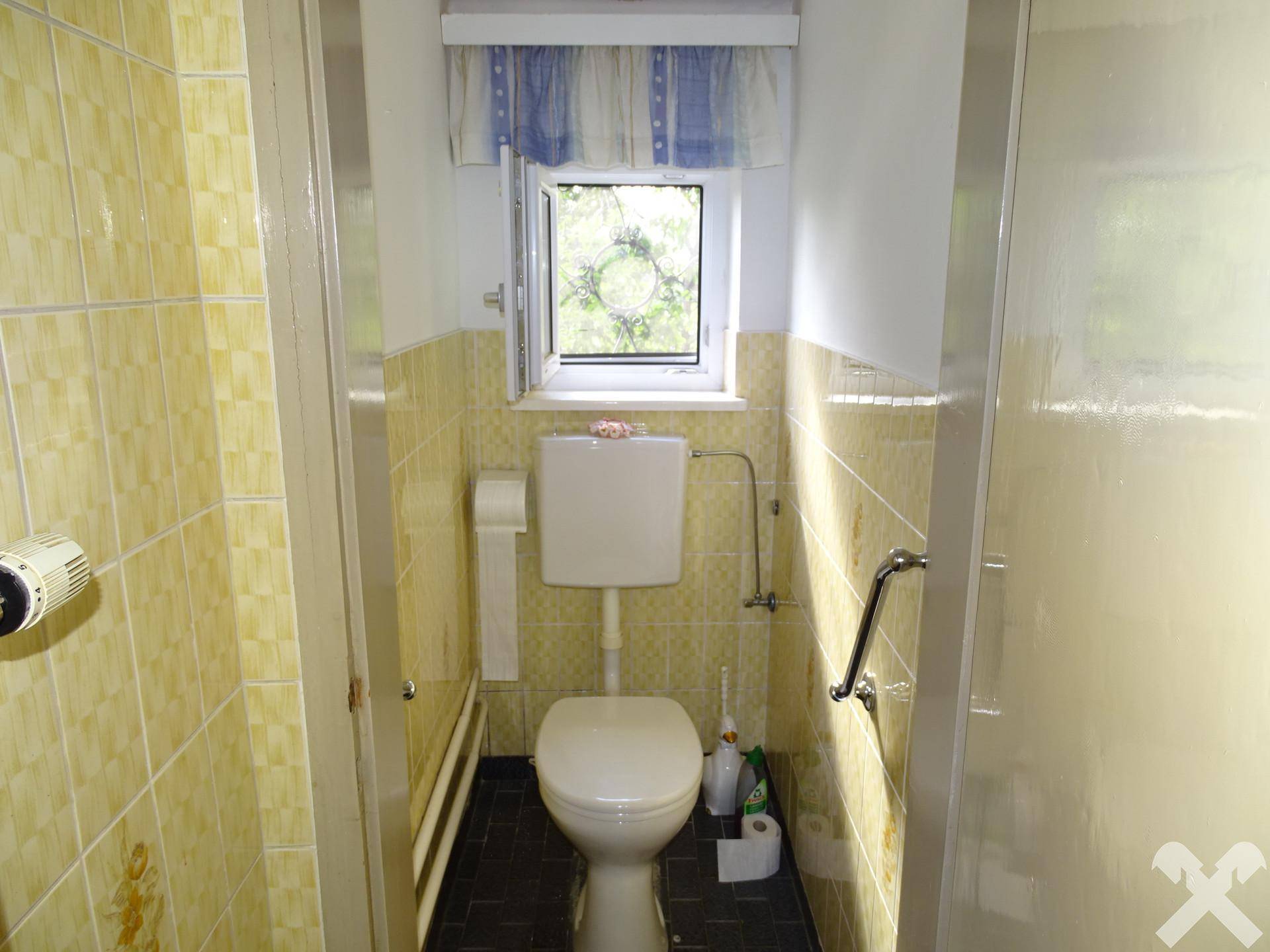 Kleines WC mit gelben Fliesen, Toilette und einem Fenster für natürliche Belüftung und Helligkeit.