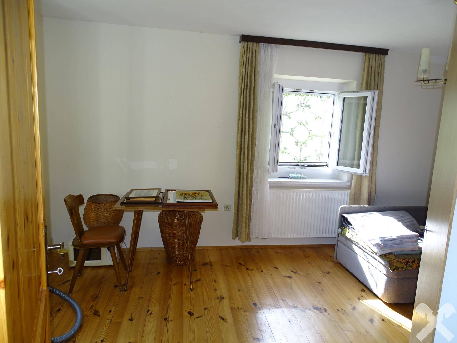 Helles Zimmer mit Holzboden, großem Fenster und einfacher Einrichtung, ideal als Schlaf- oder Gästezimmer.