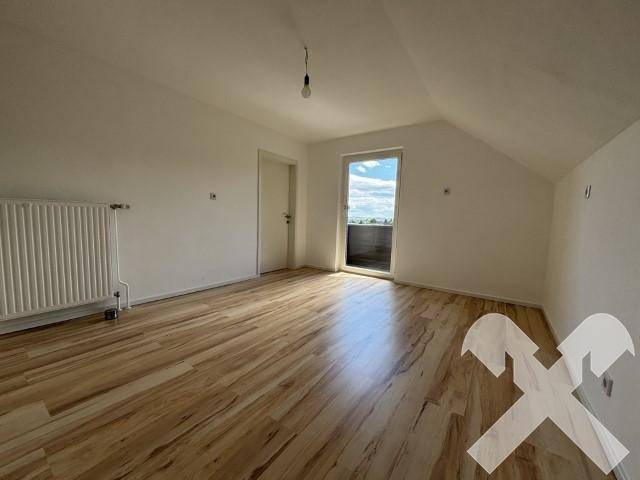 Helles Zimmer im Dachgeschoss mit Laminatboden und Zugang zu einem kleinen Balkon.