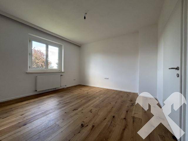 Geräumiges Zimmer mit Holzboden und großem Fenster, ideal als Schlaf- oder Arbeitszimmer.