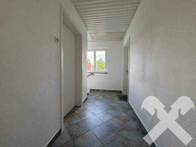 Heller Flur mit Fliesenboden und Fenster am Ende, das Tageslicht hereinlässt.