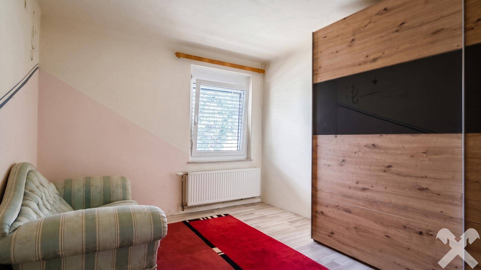 Schlafzimmer mit Holzschrank, einem Sofa und einem Fenster mit Blick ins Grüne.