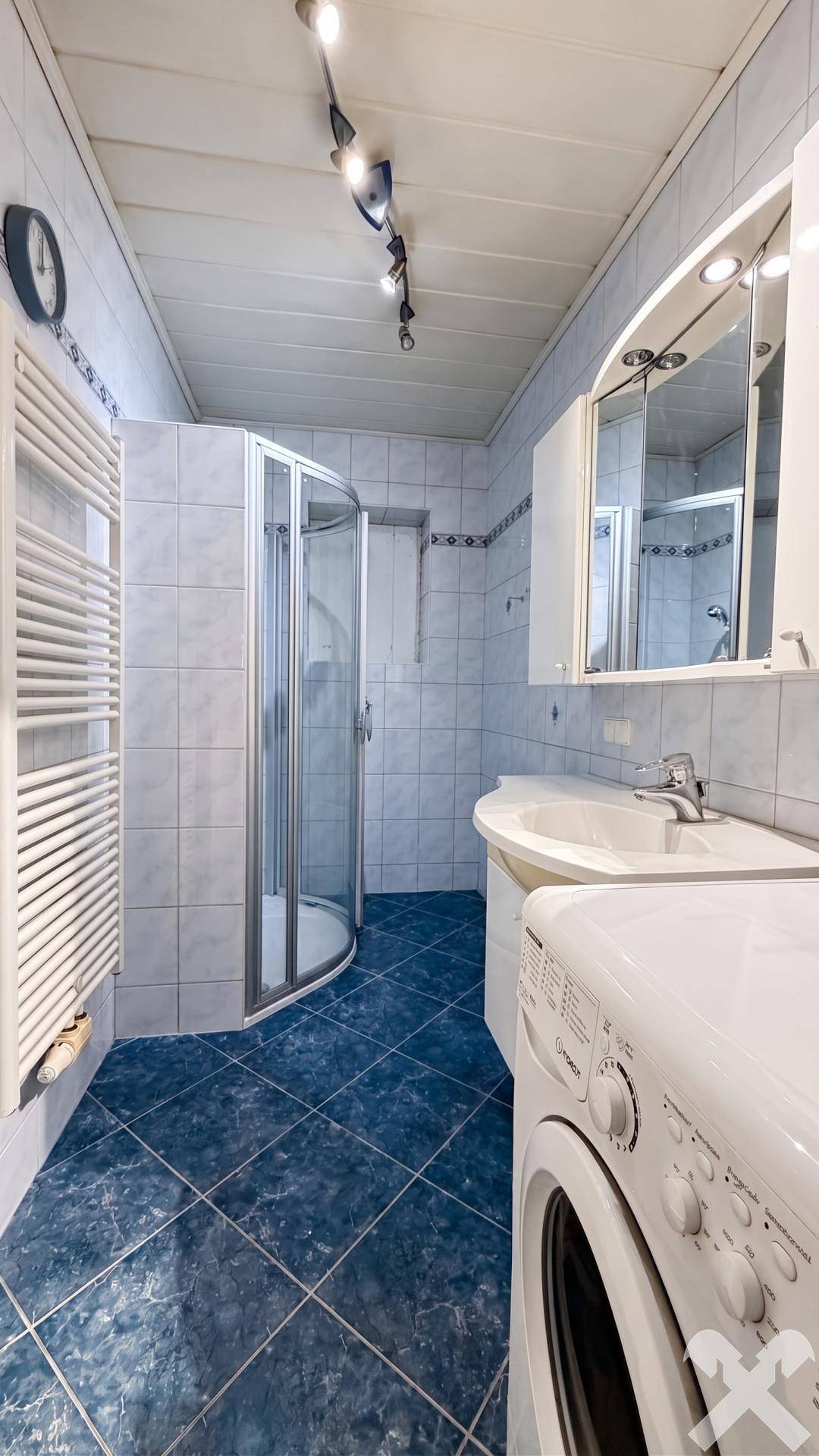 Badezimmer mit blauen Fliesen, Duschkabine, Waschbecken und Waschmaschine.