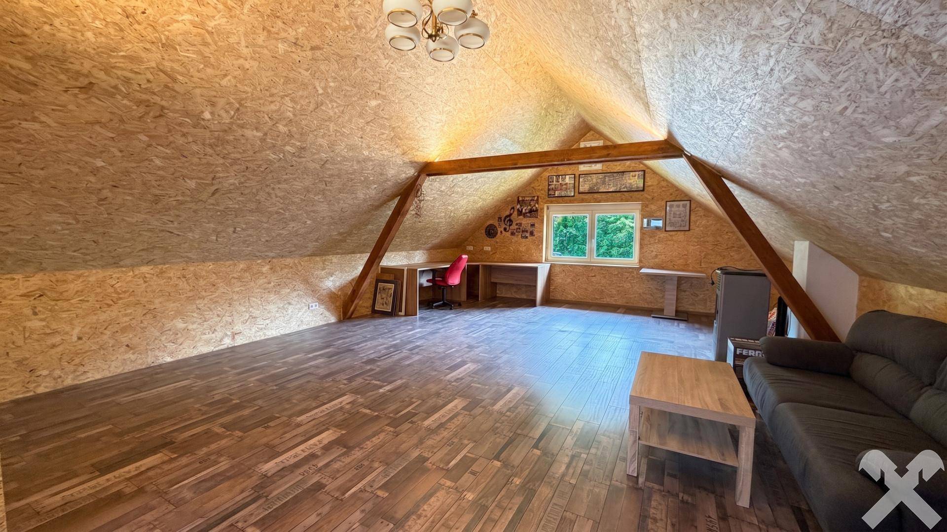 Ausgebauter Dachboden mit Holzverkleidung, Holzbalken und einem Fenster.