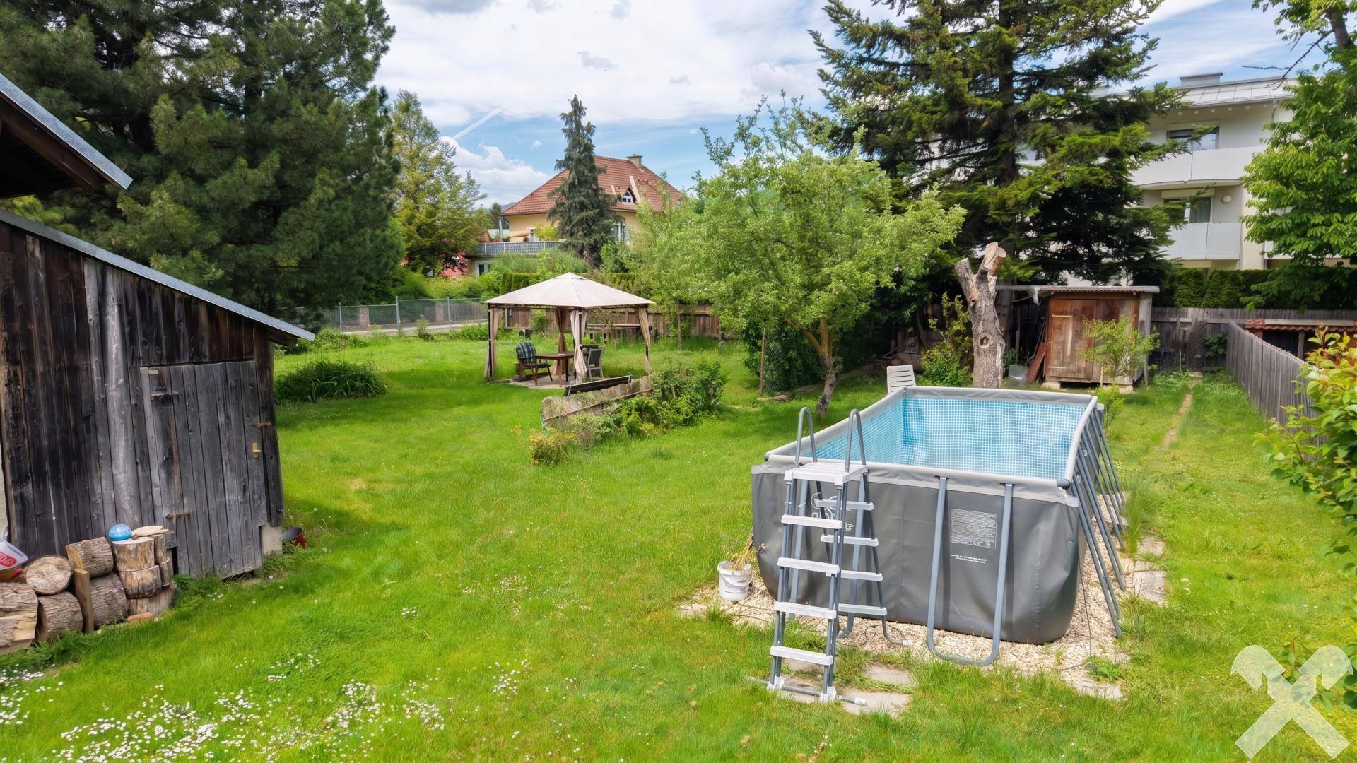 Großer Garten mit Rasenfläche, Aufstellpool und einem Pavillon im Hintergrund.