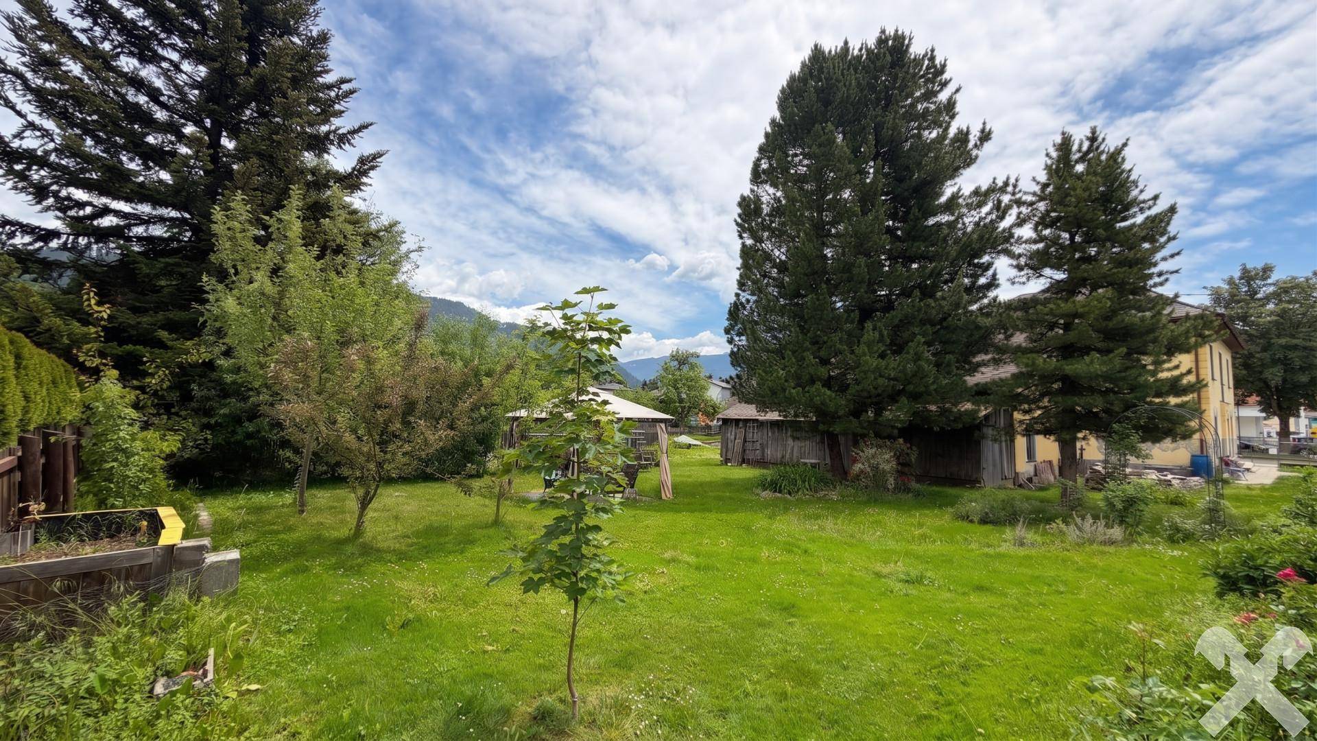 Weitläufiger Garten mit Rasen, jungen Bäumen und Blick auf die umliegende Landschaft.