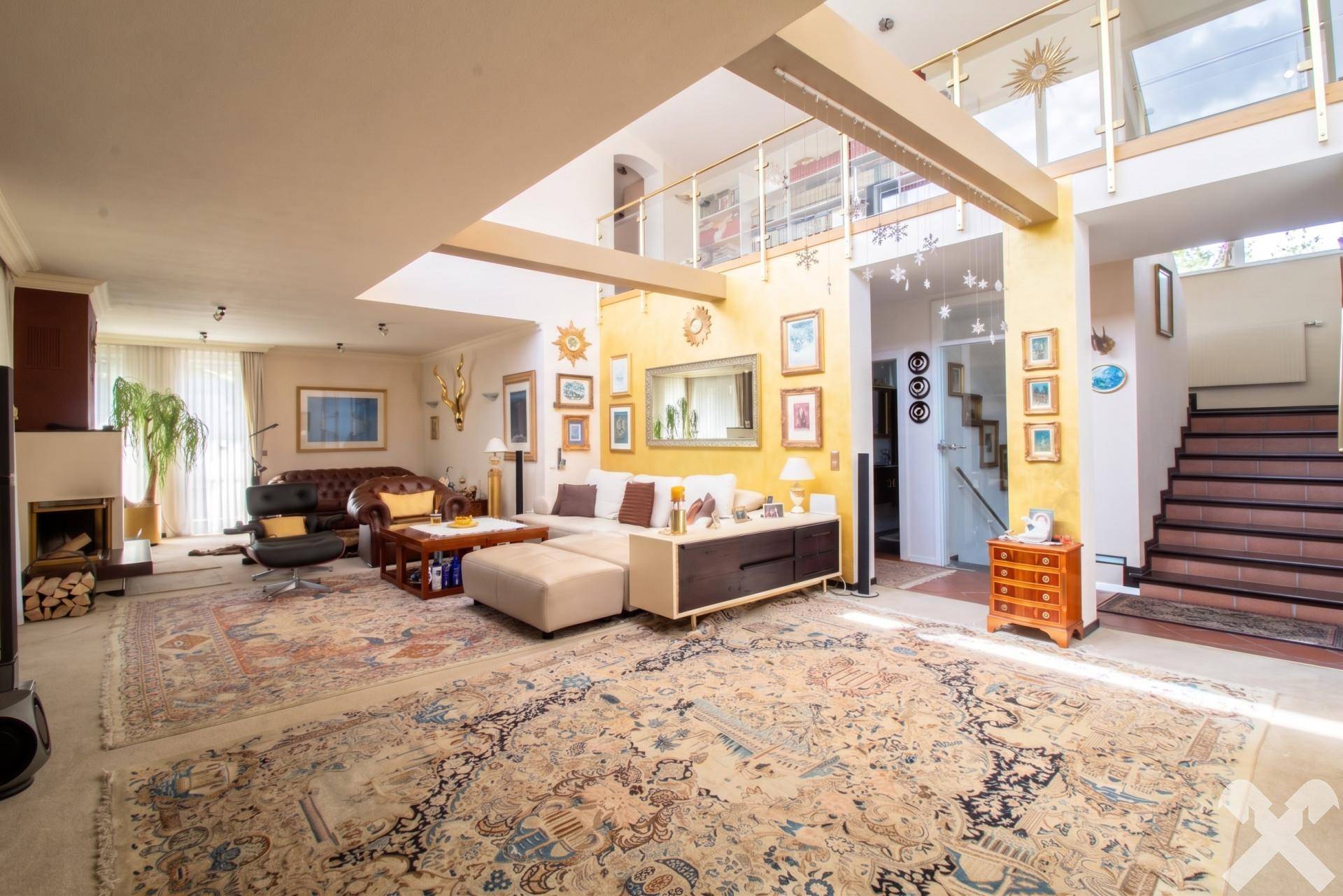 Großzügiges Wohnzimmer mit hohen Decken, Kamin und opulenten Teppichen, offen zur Galerie.