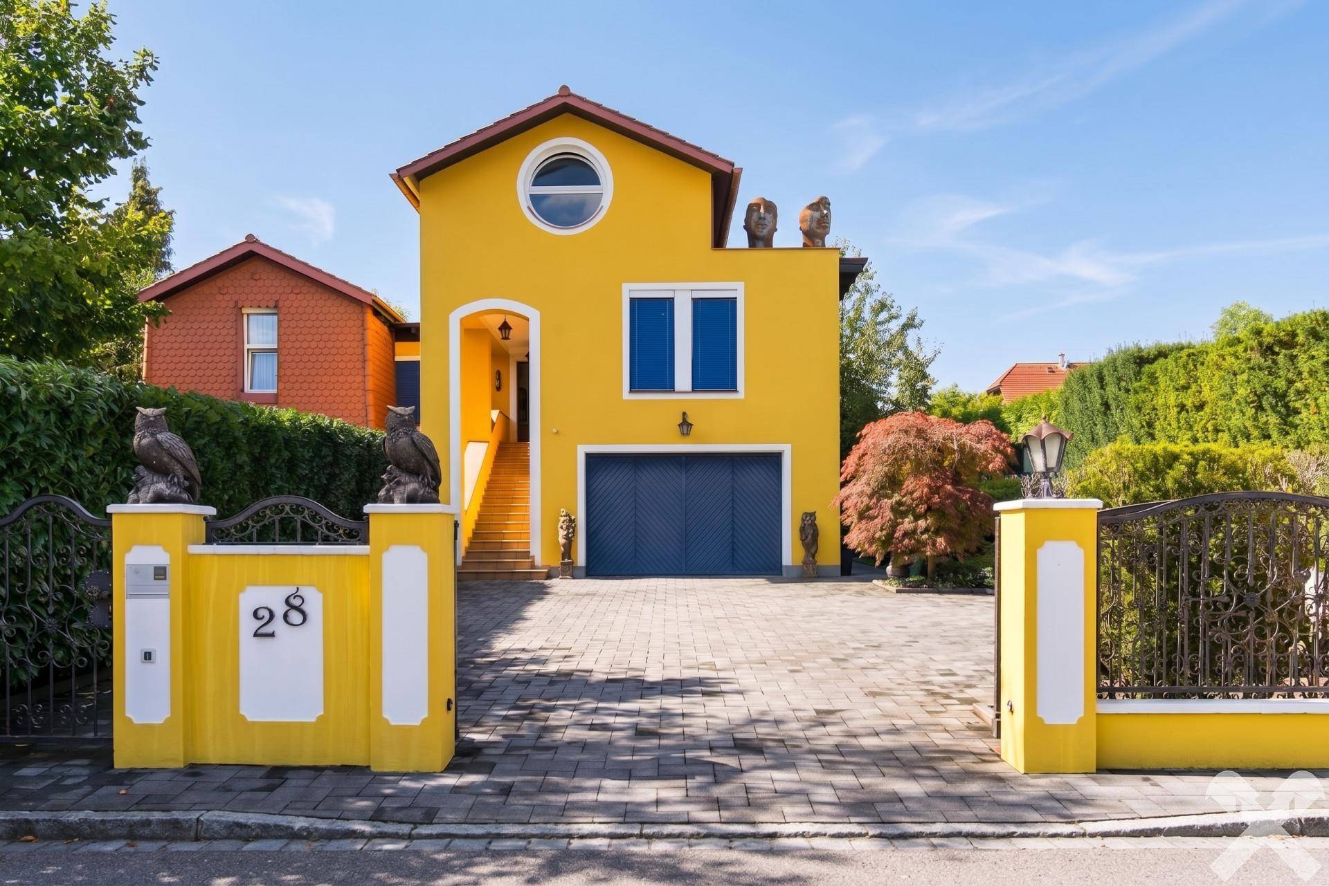 Vorderansicht des gelben Hauses mit Eingangstor, Hausnummer 28 und dekorativen Eulenstatuen.