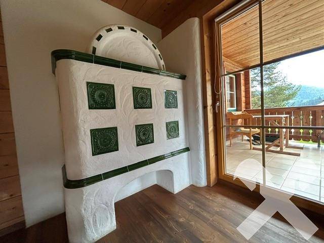 Detailansicht des traditionellen Kachelofens mit grünen Fliesen und Zugang zum Balkon.