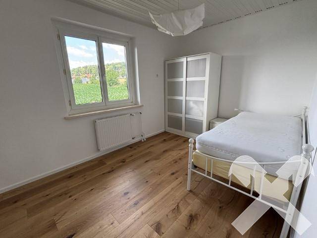 Helles Schlafzimmer mit Holzboden, Fenster und Blick ins Grüne.
