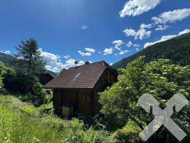 Charmantes Holzhaus eingebettet in eine idyllische Berglandschaft unter blauem Himmel.