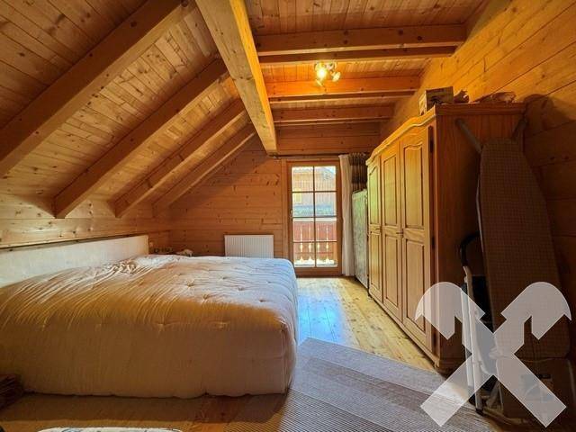 Helles Schlafzimmer im Dachgeschoss mit Holzbalken, großem Bett und Zugang zum Balkon.