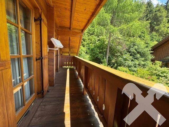 Langer Holzbalkon mit traditionellem Geländer und Blick auf die umliegenden Bäume.