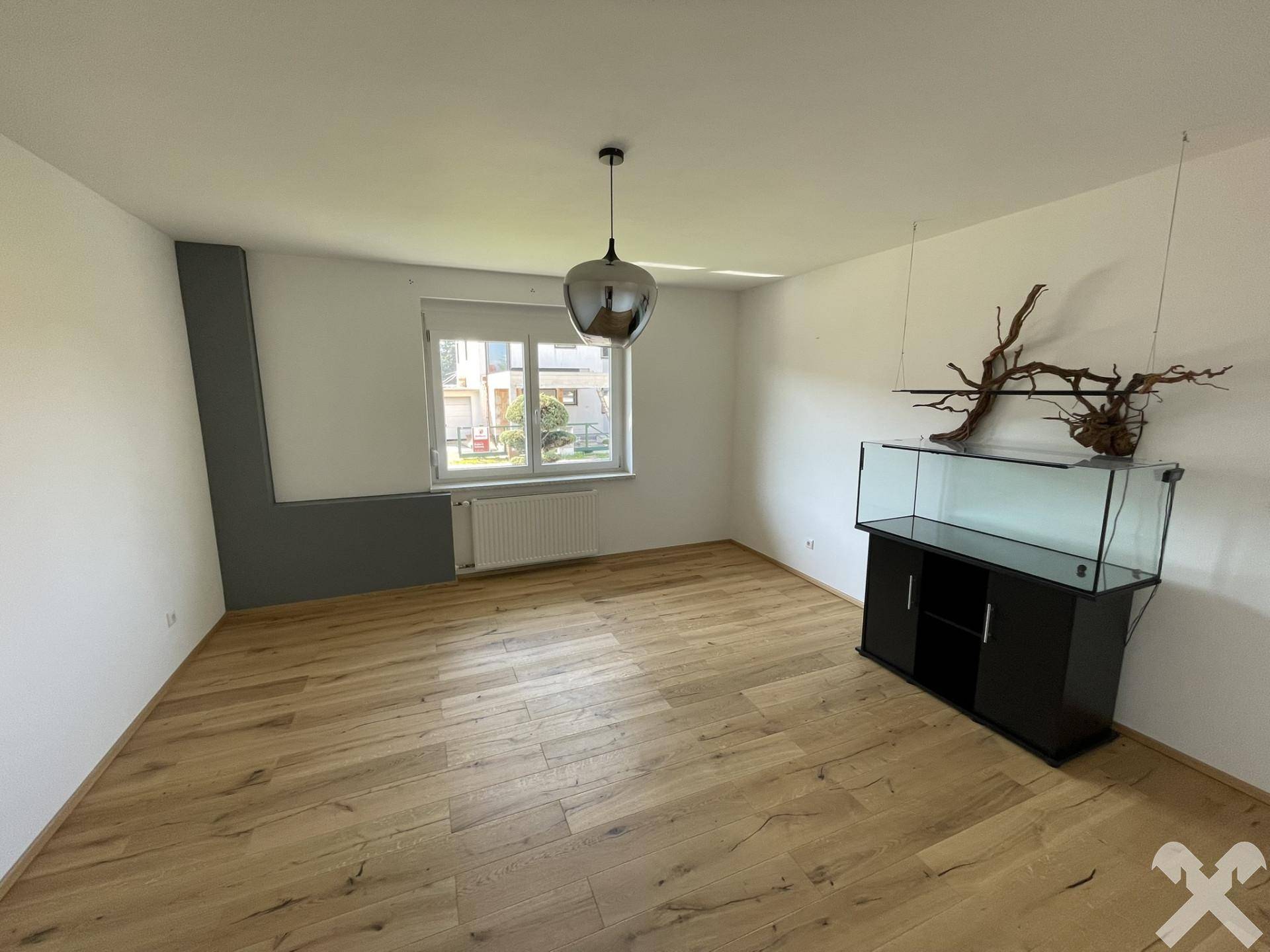 Helles Wohnzimmer mit Holzboden, großem Fenster und einem Aquarium als Dekoration.