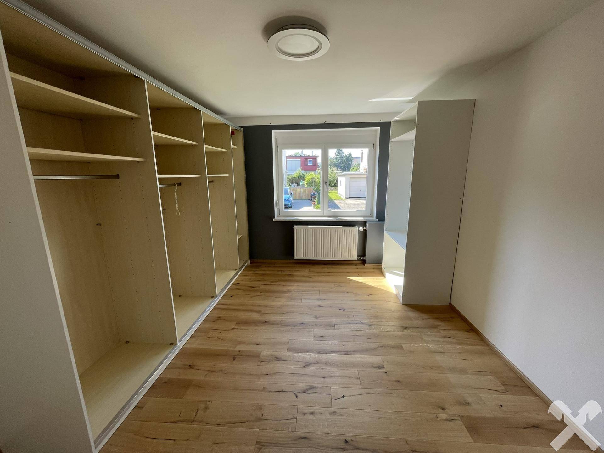 Geräumiges Schlafzimmer mit Holzboden, großem Fenster und eingebauten Kleiderschränken.