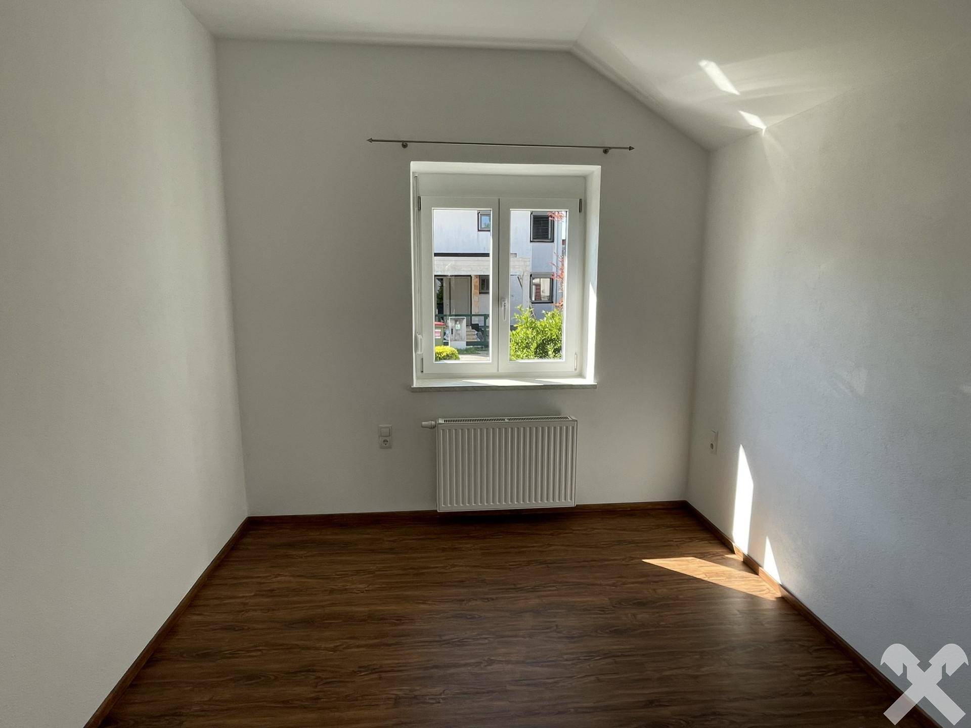 Helles Schlafzimmer mit Holzboden, Dachschräge und Fenster mit Blick ins Grüne.