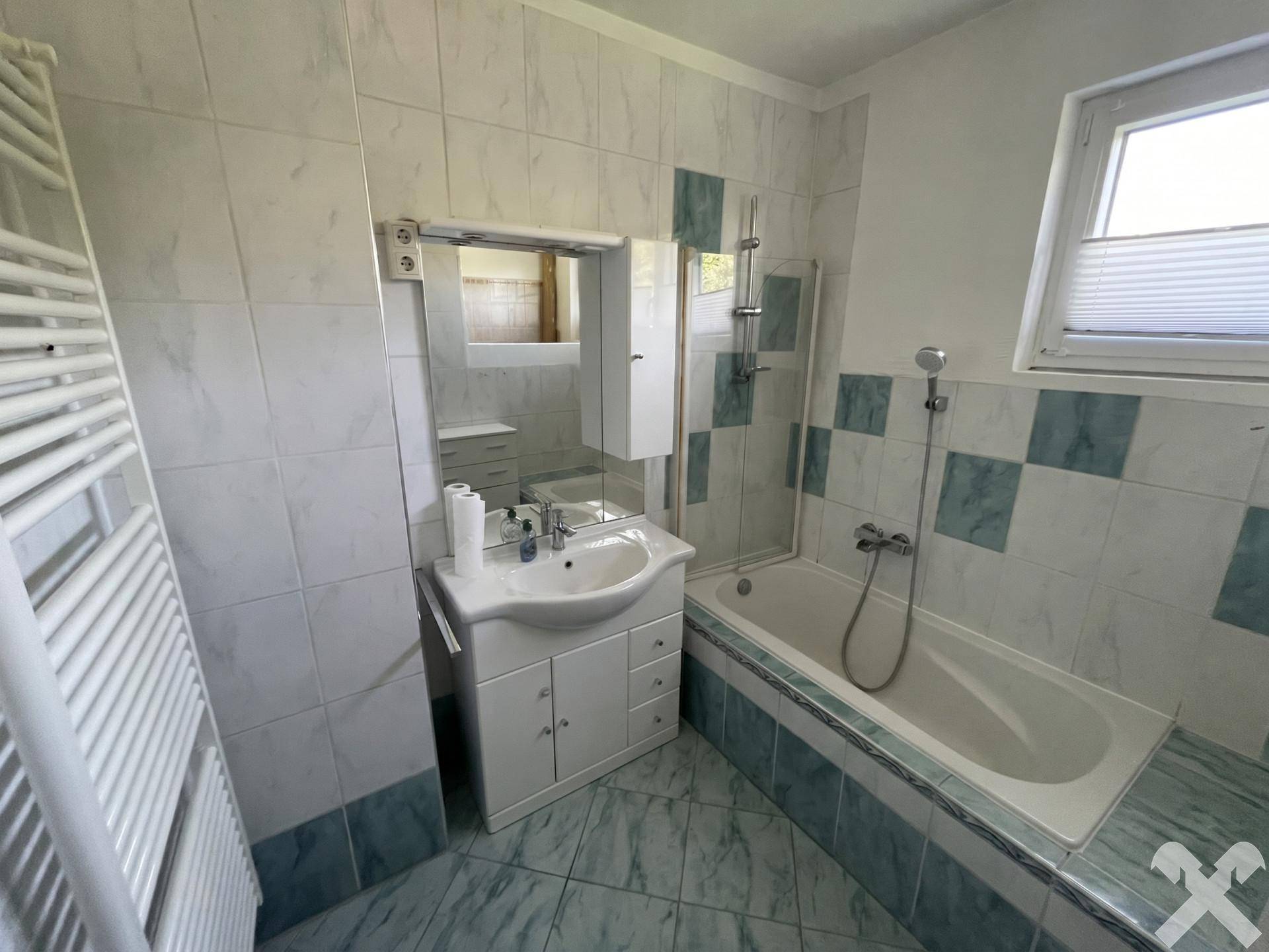 Badezimmer mit Badewanne, Waschbecken und Fliesen in hellblauen und weißen Farbtönen.