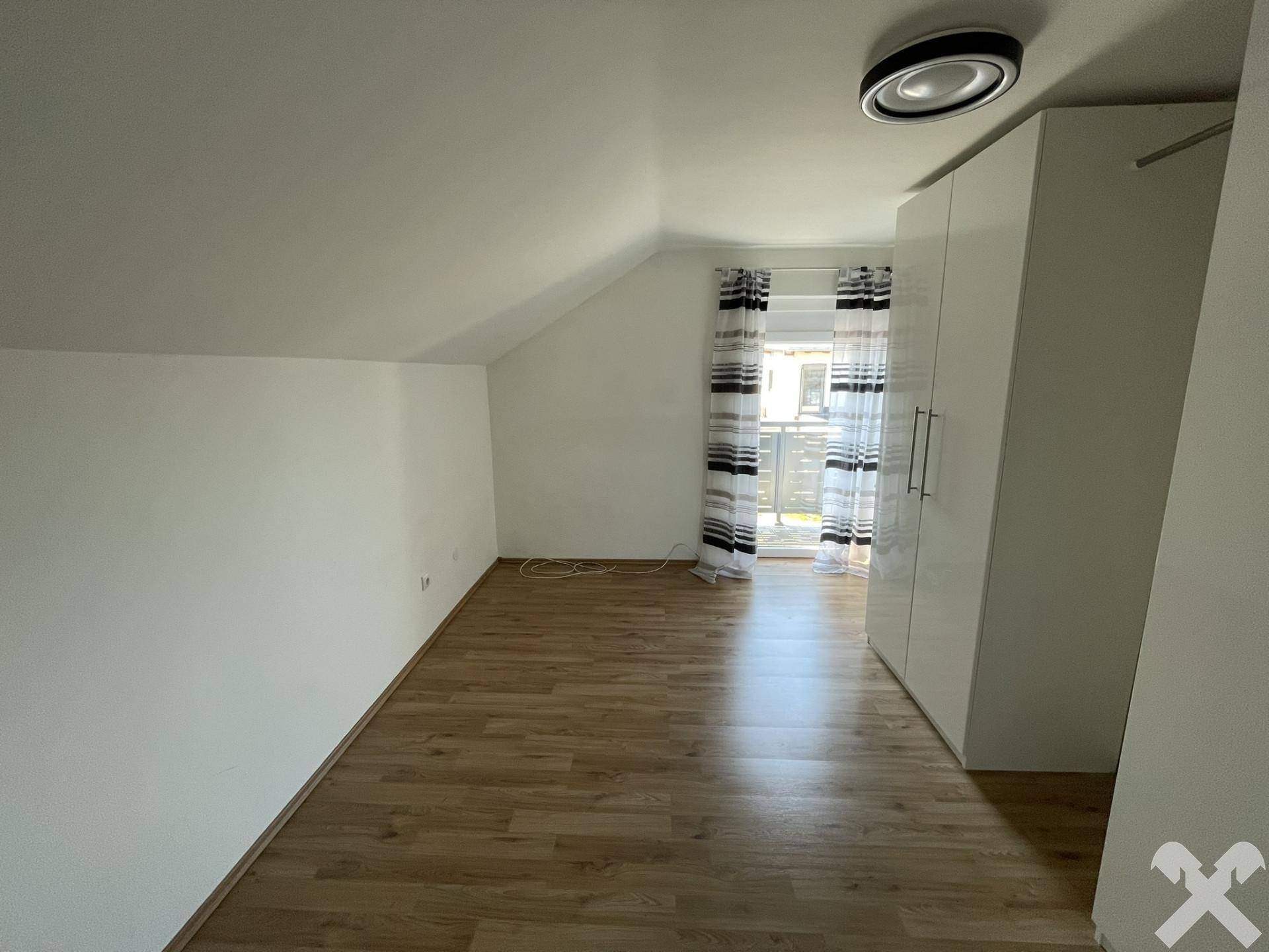 Schlafzimmer im Dachgeschoss mit Holzboden, Dachschräge und großem Kleiderschrank.