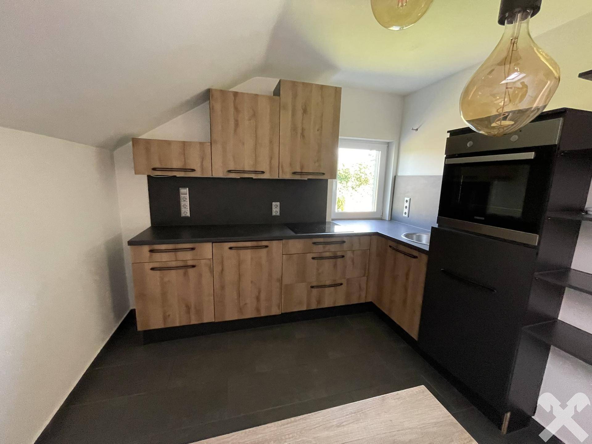Moderne Einbauküche im Dachgeschoss mit Holzoptik-Fronten und dunkler Arbeitsplatte.