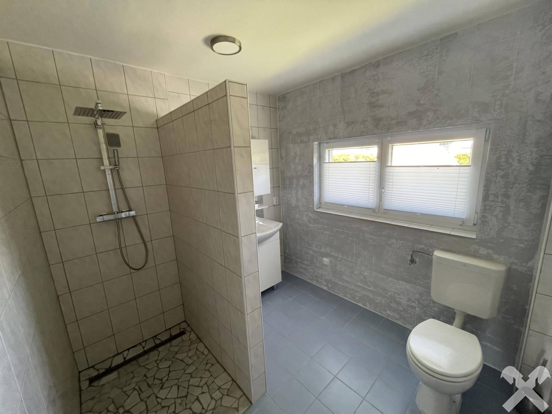 Modernes Badezimmer mit ebenerdiger Dusche, WC und Fenster für Tageslicht.