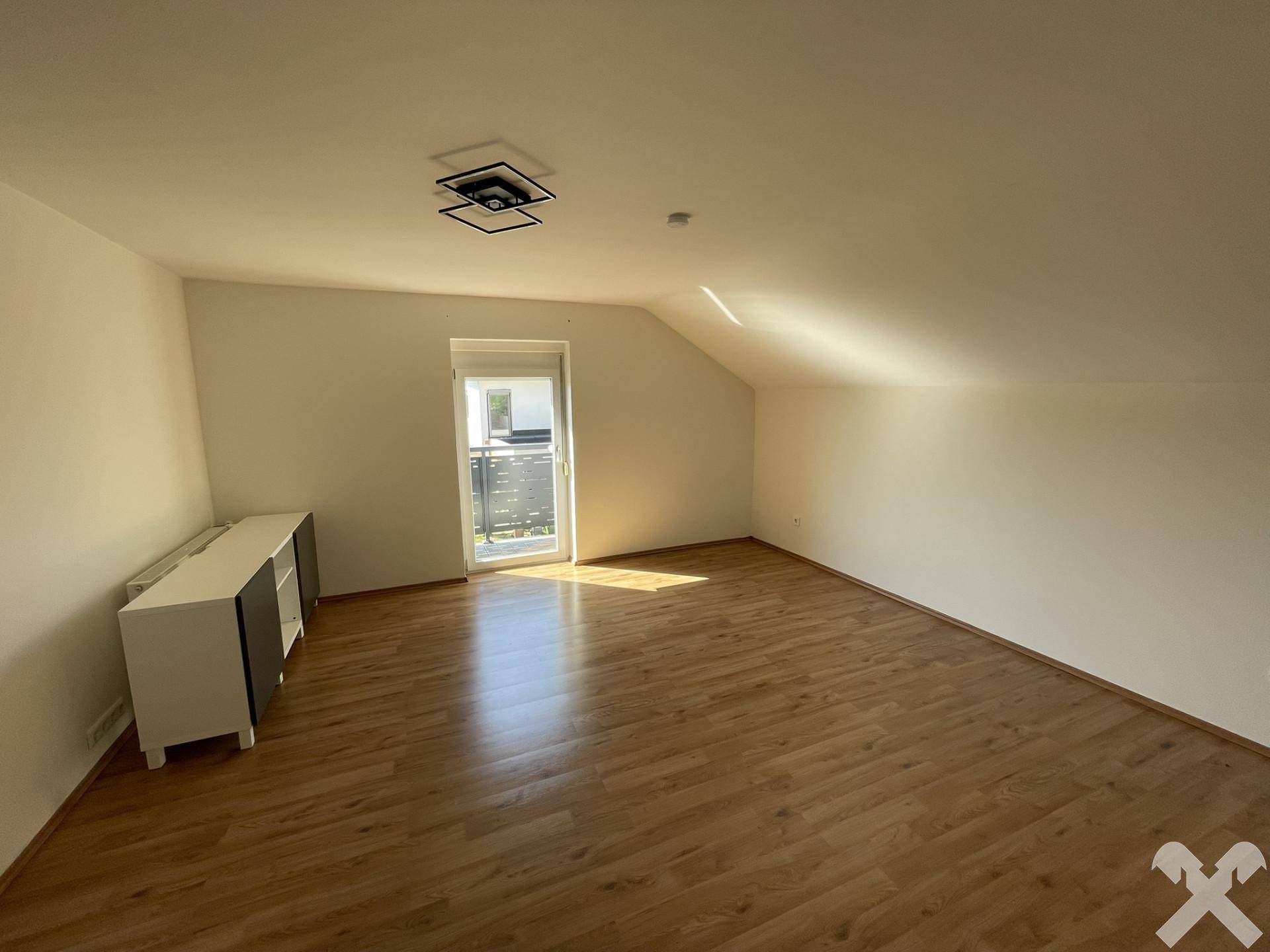 Geräumiges Schlafzimmer mit Holzboden, Dachschräge und Zugang zu einem französischen Balkon.