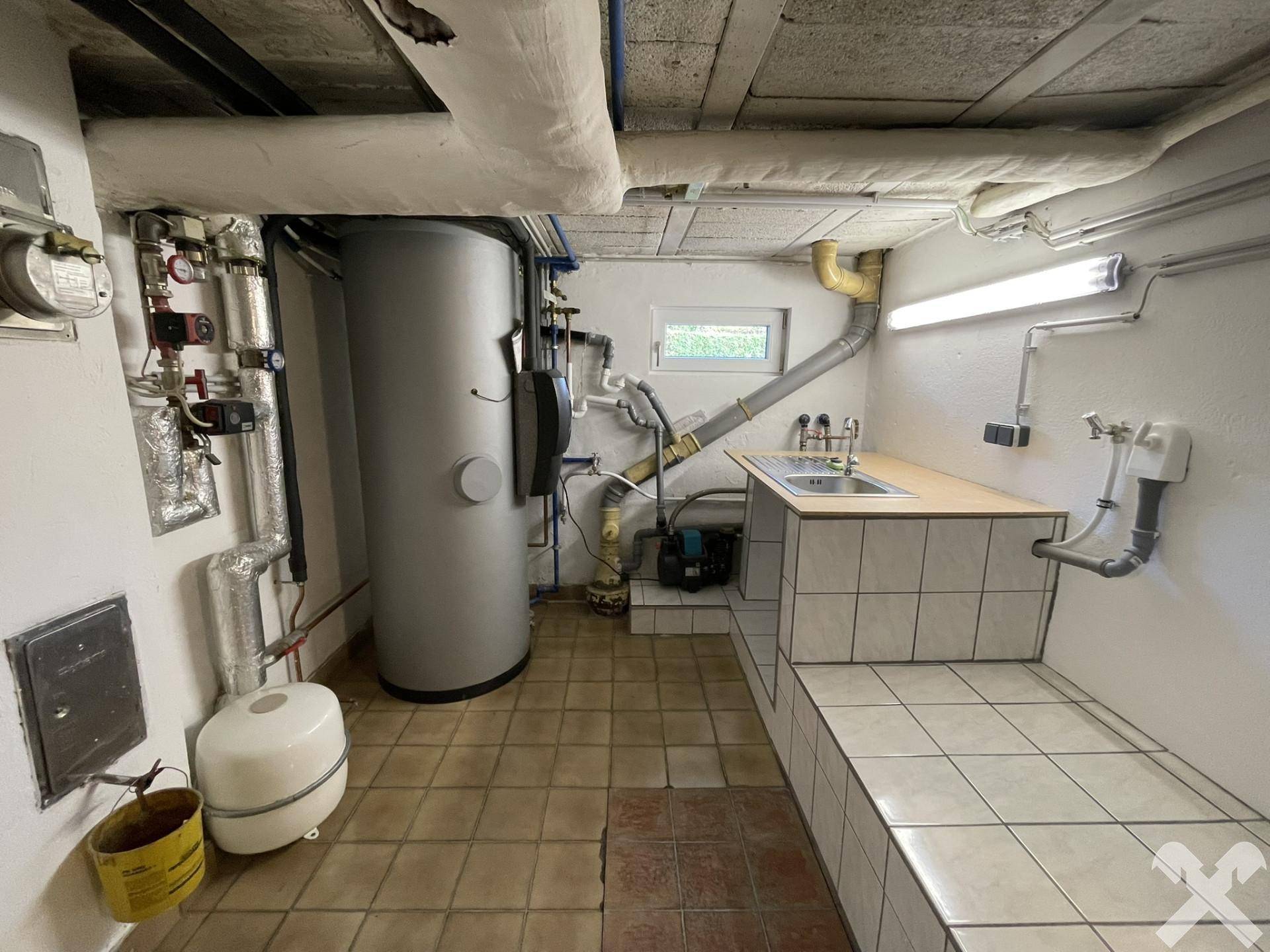 Technikraum im Keller mit Heizungsanlage, Warmwasserspeicher und Waschbecken.