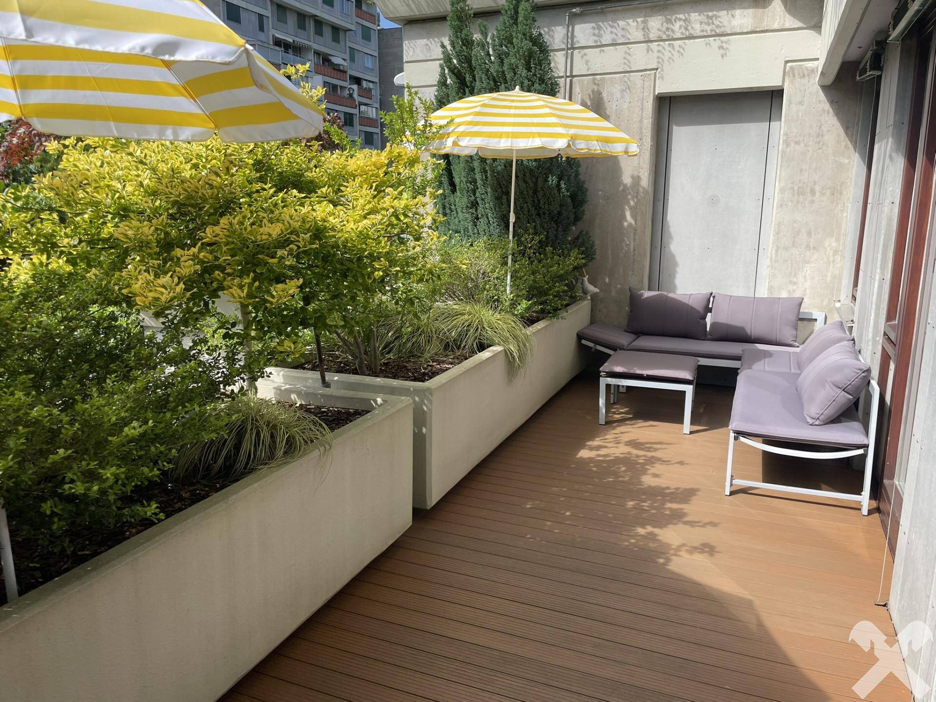 Geräumige Terrasse mit Holzdeck, Pflanzenkübeln und bequemen Outdoor-Sitzmöbeln.