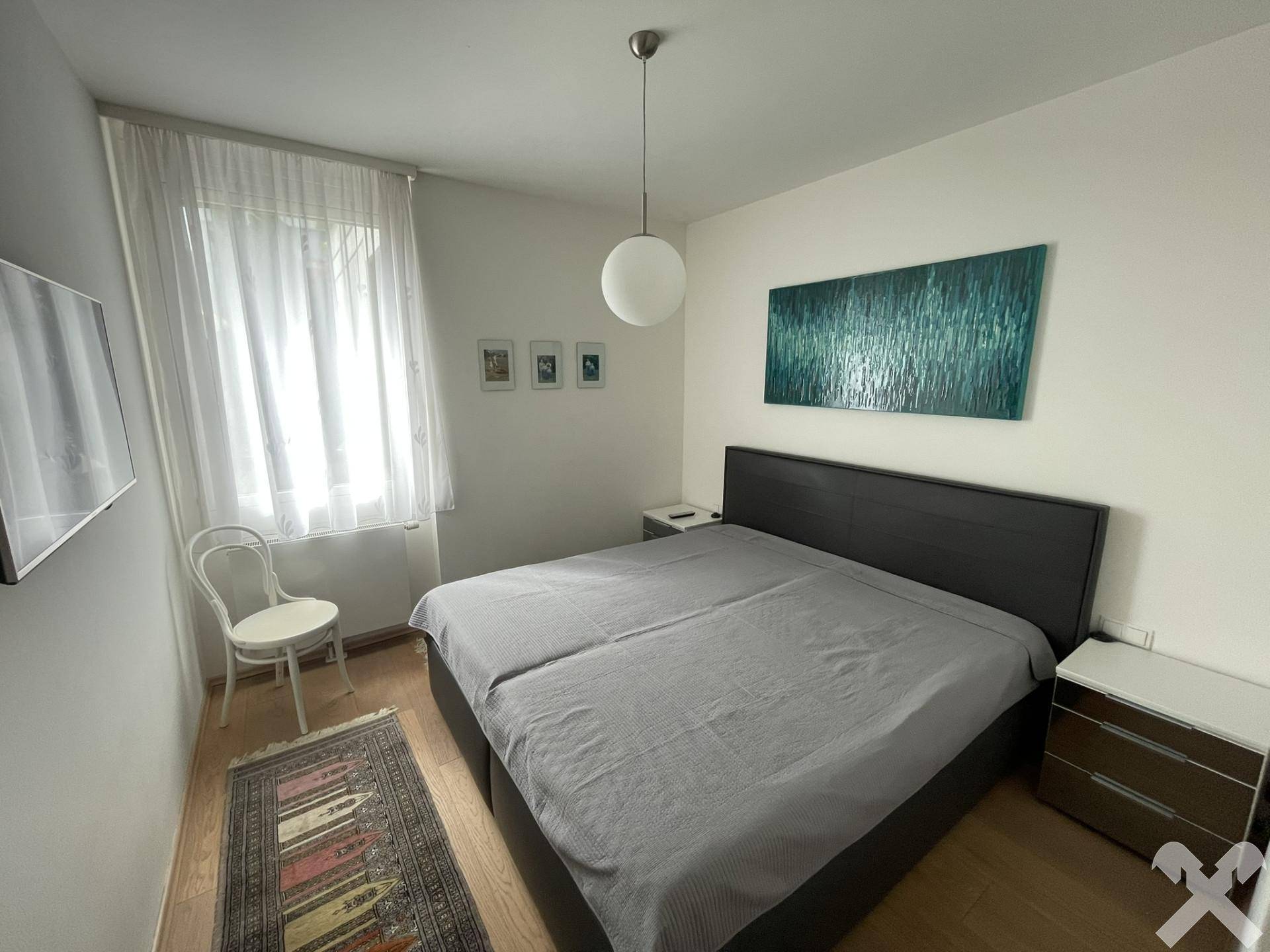 Gemütliches Schlafzimmer mit Doppelbett, Holzparkett und einem Fenster mit Vorhängen.