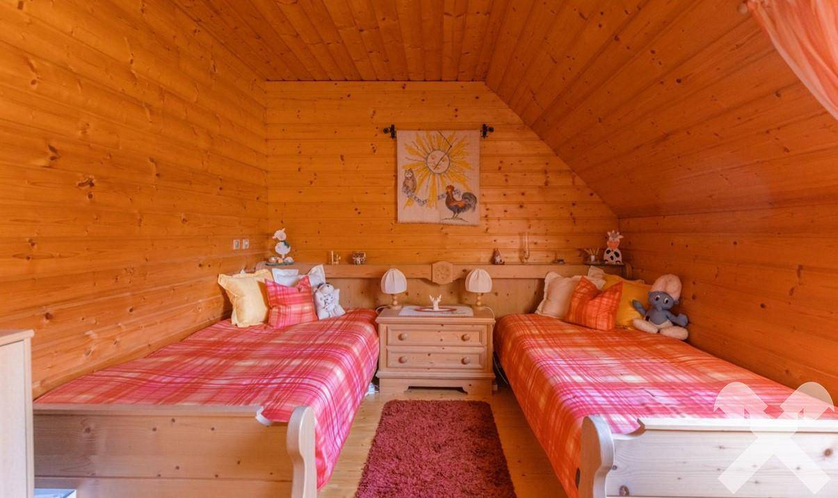 Kinderzimmer im Dachgeschoss mit zwei Einzelbetten, Holzwänden und farbenfroher Dekoration.