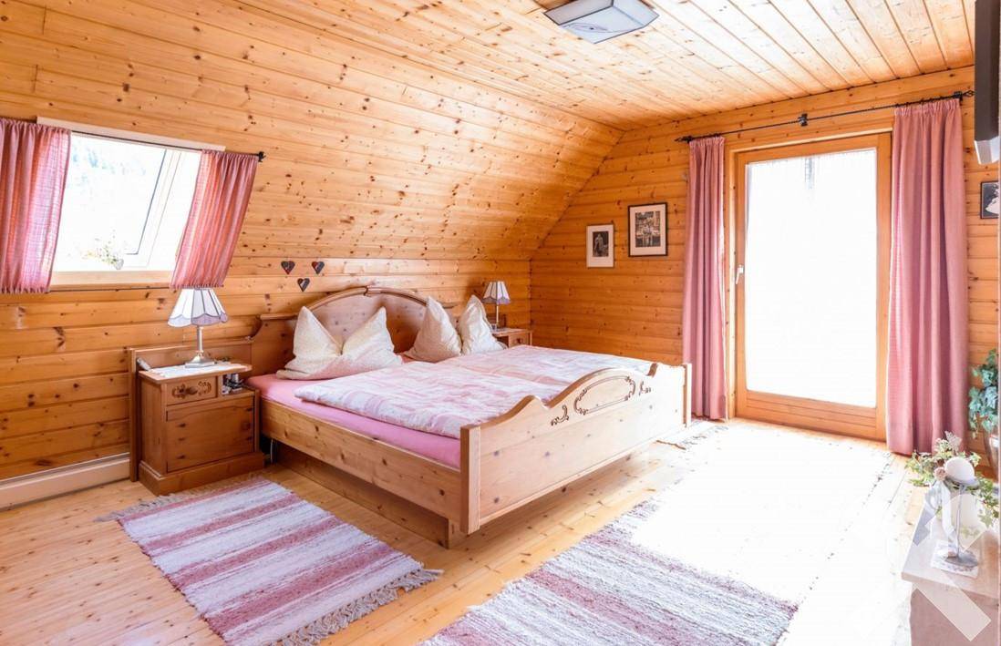 Helles Schlafzimmer mit Holzwänden, Doppelbett und Zugang zu einem Balkon.