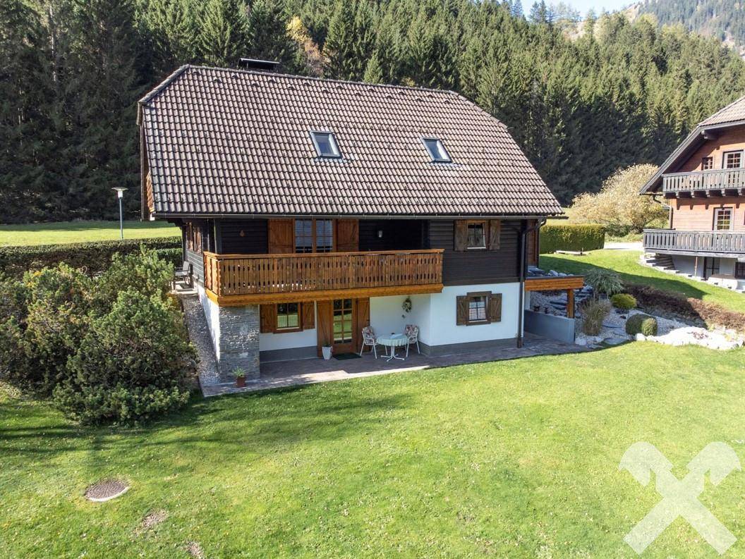 Charmantes Holzhaus mit mehreren Balkonen und einer kleinen Terrasse, eingebettet in eine grüne Landschaft.