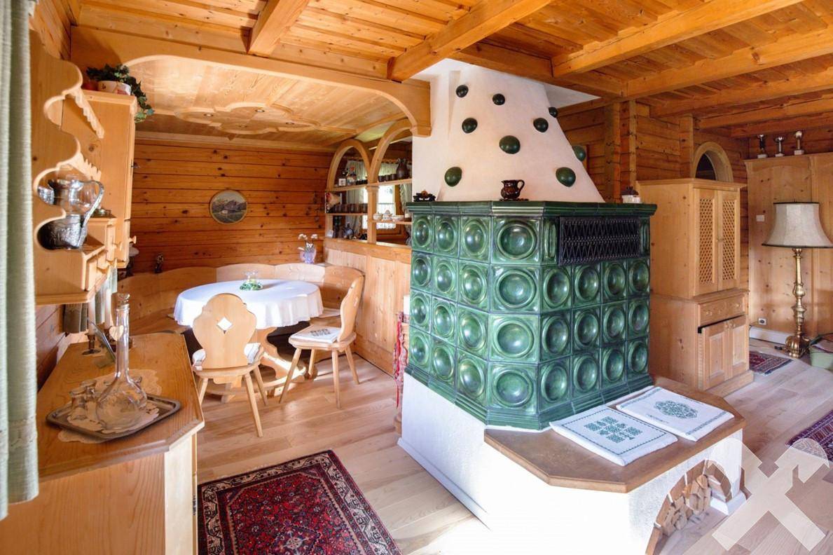 Traditioneller Essbereich mit Holztisch, Stühlen und einem markanten grünen Kachelofen.