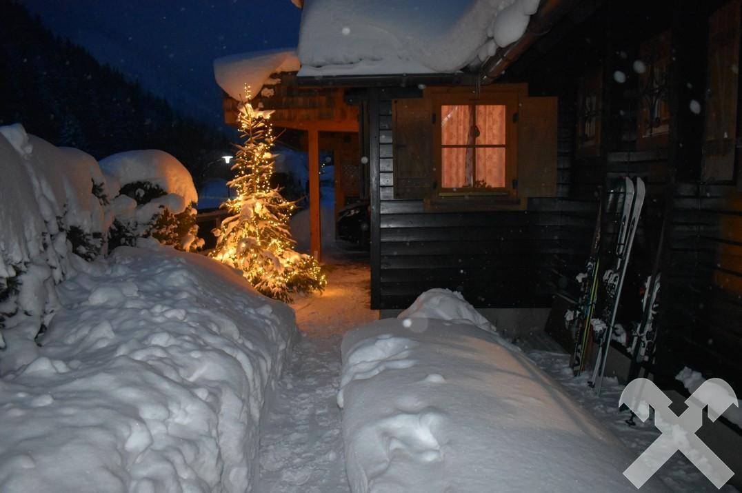 Verschneiter Eingangsbereich eines Holzhauses bei Nacht, festlich beleuchtet.