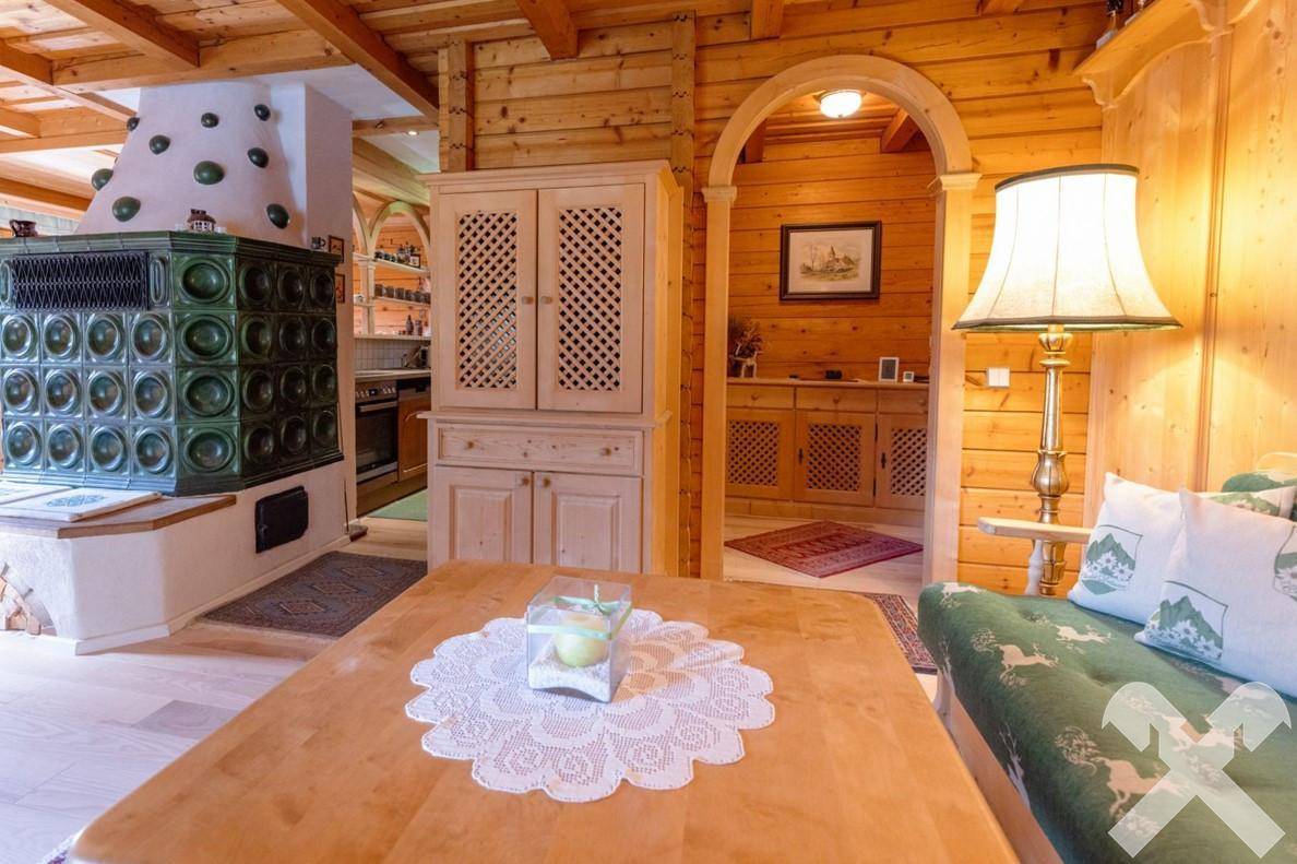 Gemütlicher Wohnbereich mit Kachelofen und einem Durchgang zu weiteren Räumen im Holzhaus.