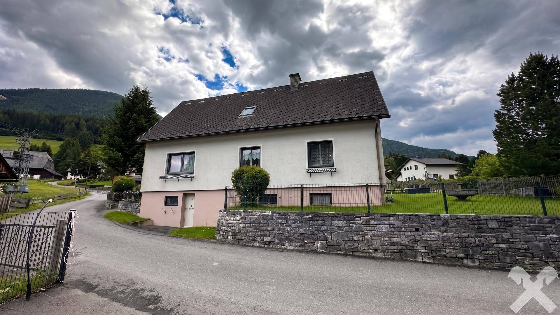 Hausansicht von der Straße mit Natursteinmauer und Blick auf die umliegende Berglandschaft.