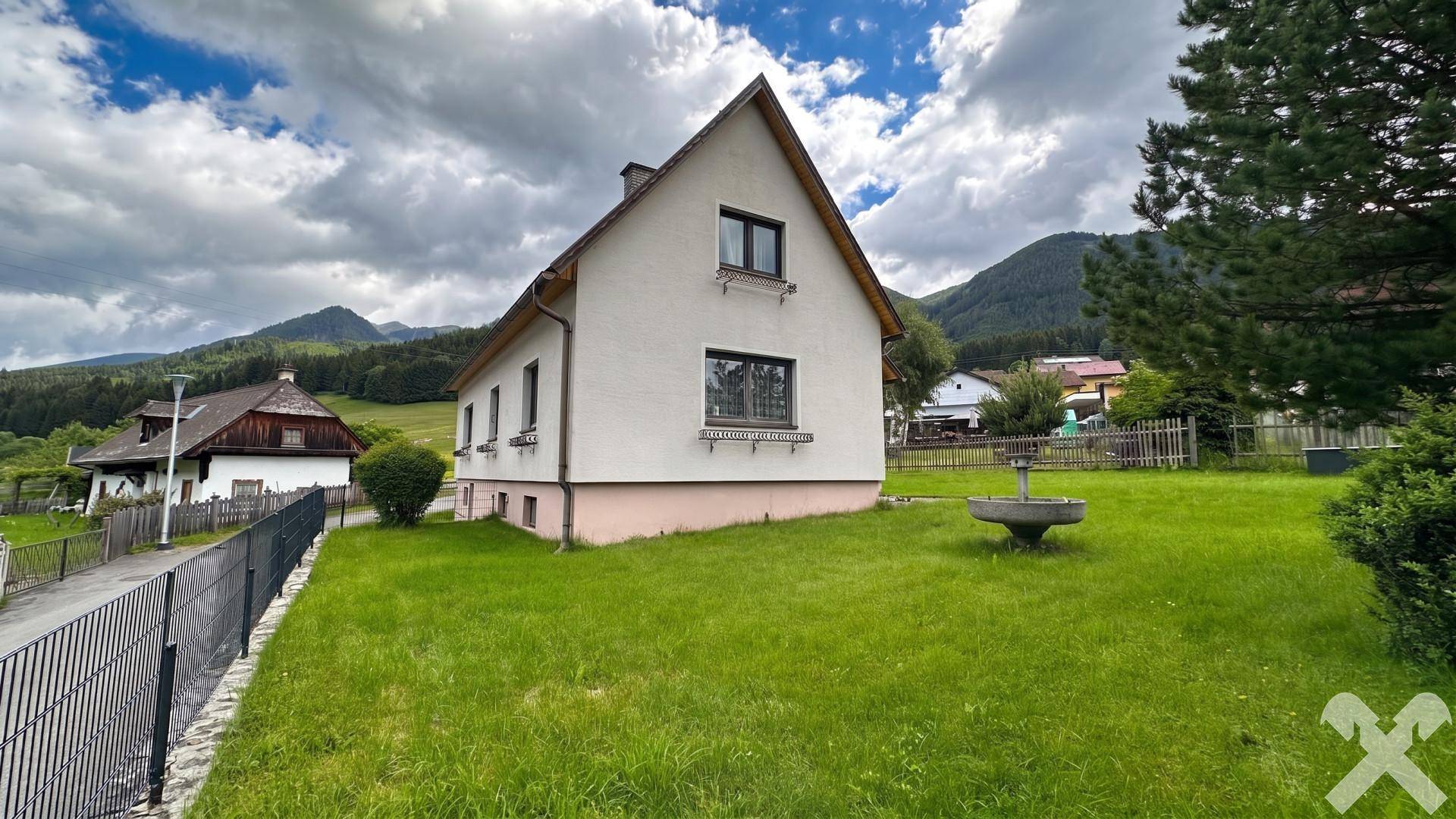 Seitenansicht des Hauses mit gepflegtem Rasen und dekorativem Brunnen im Vorgarten.