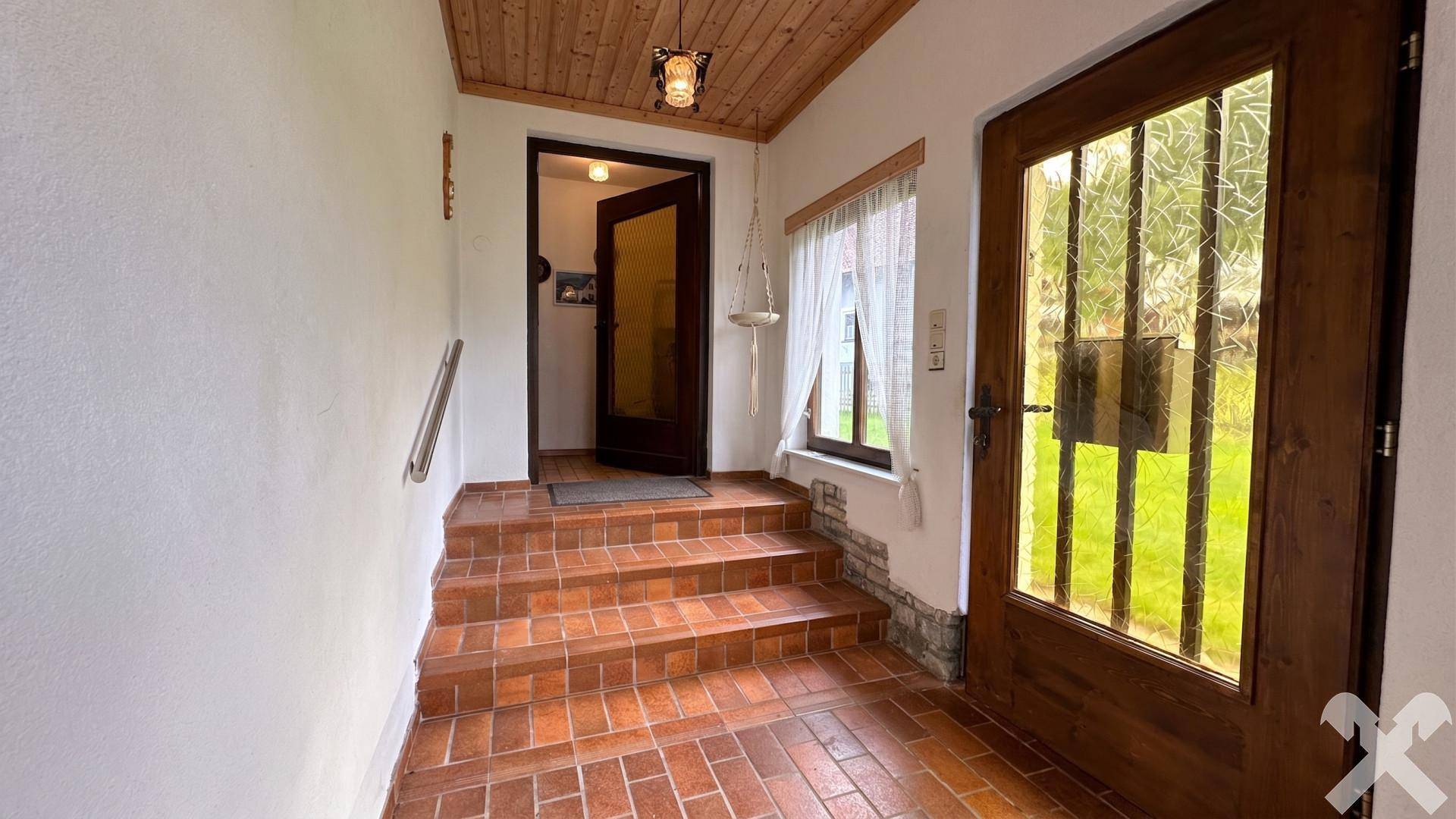 Eingangsbereich mit Terrakotta-Fliesenstufen, Holzdecke und rustikaler Holztür.